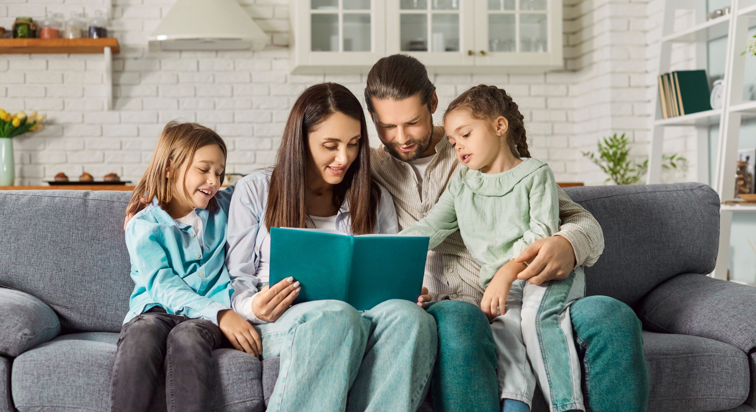 A family sitting together on a couch reading a book, representing the crucial role of parental engagement in supporting a child's social development.